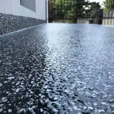 Nowoczesna żywica na balkon cena za metr. Ciemna, błyszcząca powierzchnia z białymi płatkami, idealna na taras.