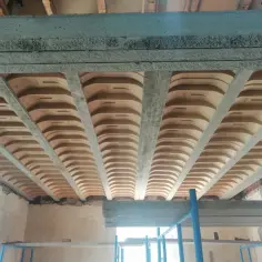 Widok od dołu na betonowe belki i pustaki, tworzące różne rodzaje stropów. Konstrukcja w trakcie budowy.