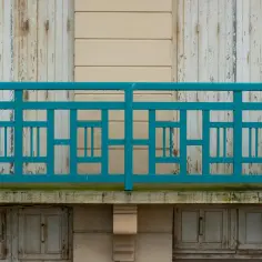 Turkusowe, geometryczne mocowanie balustrady od czoła na tle starych, drewnianych drzwi i jasnej ściany.