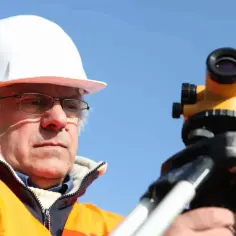 Geodeta w kasku i kamizelce odmierza teren. Zastanawiasz się, ile geodeta bierze od punktu?