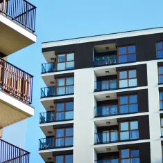 Nowoczesne budynki z loggią i balkonem, z przeszklonymi balustradami i drewnianymi ramami okien, na tle błękitnego nieba.