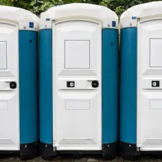 Trzy niebiesko-białe toalety przenośne ustawione obok siebie. Sprawdź, jaka jest wynajem toi toi cena, aby zorganizować wydarzenie.