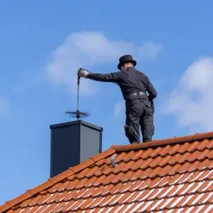 Kominiarz na dachu czyści komin. Zastanawiasz się, ile kosztuje przegląd kominiarski?