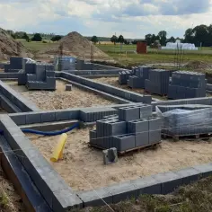 Budowa fundamentów domu w toku. Betonowe bloki i piasek na placu budowy. Cena budowy fundamentów zależy od wielu czynników.