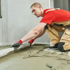 Budowlaniec wyrównuje świeży jastrych cementowy za pomocą łaty.