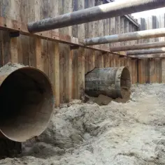 Budowa tunelu z wykorzystaniem ścianek szczelnych. Widoczne stalowe rury i wykop z piaskiem.