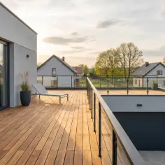 Drewniany taras nad garażem z leżakiem i widokiem na wieś.