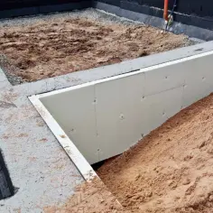 Budowa domu w toku. Widoczna izolowana stopa fundamentowa, zasypana piaskiem.