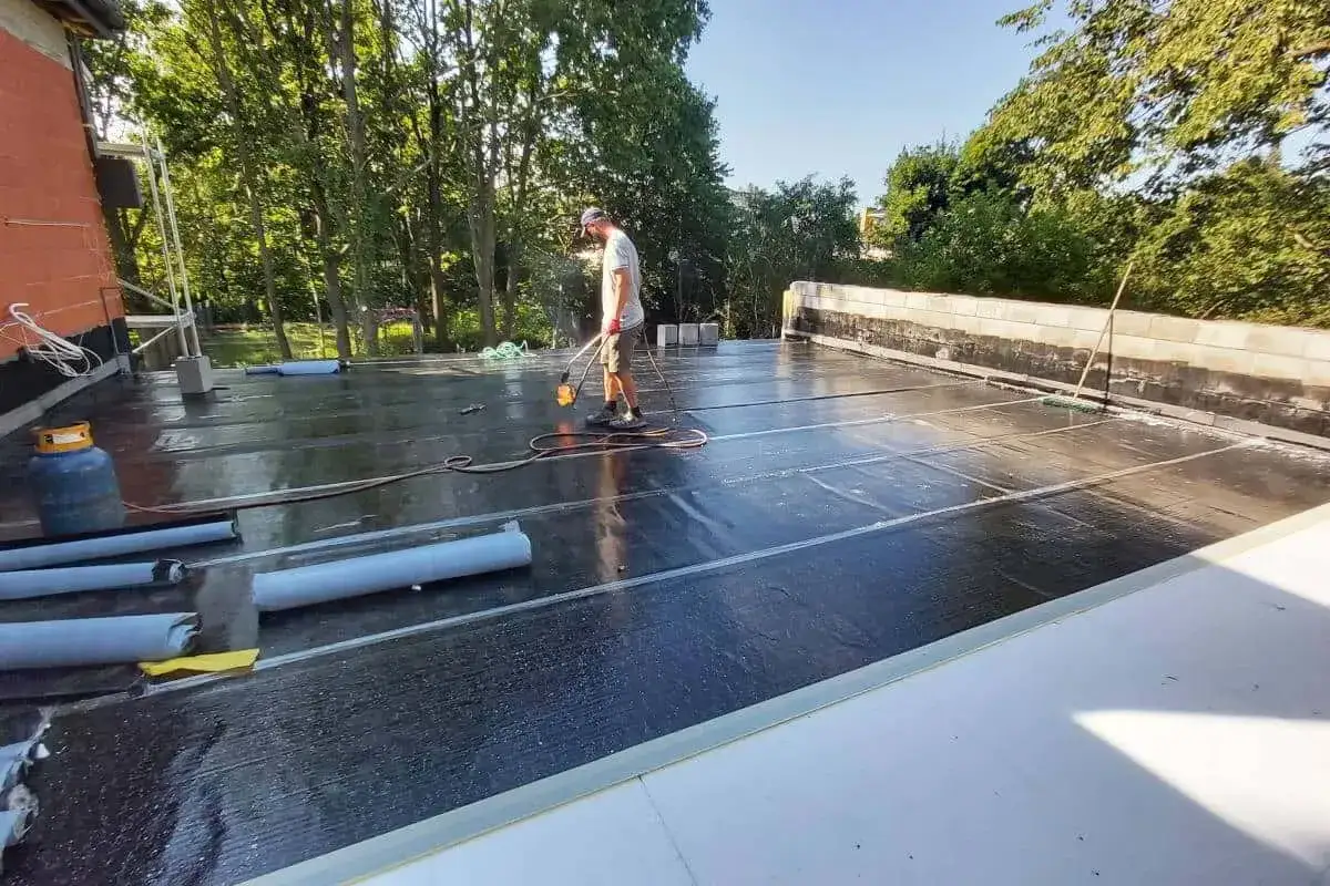 Pracownik wykonuje hydroizolację tarasu nad garażem, używając palnika do zgrzewania papy.