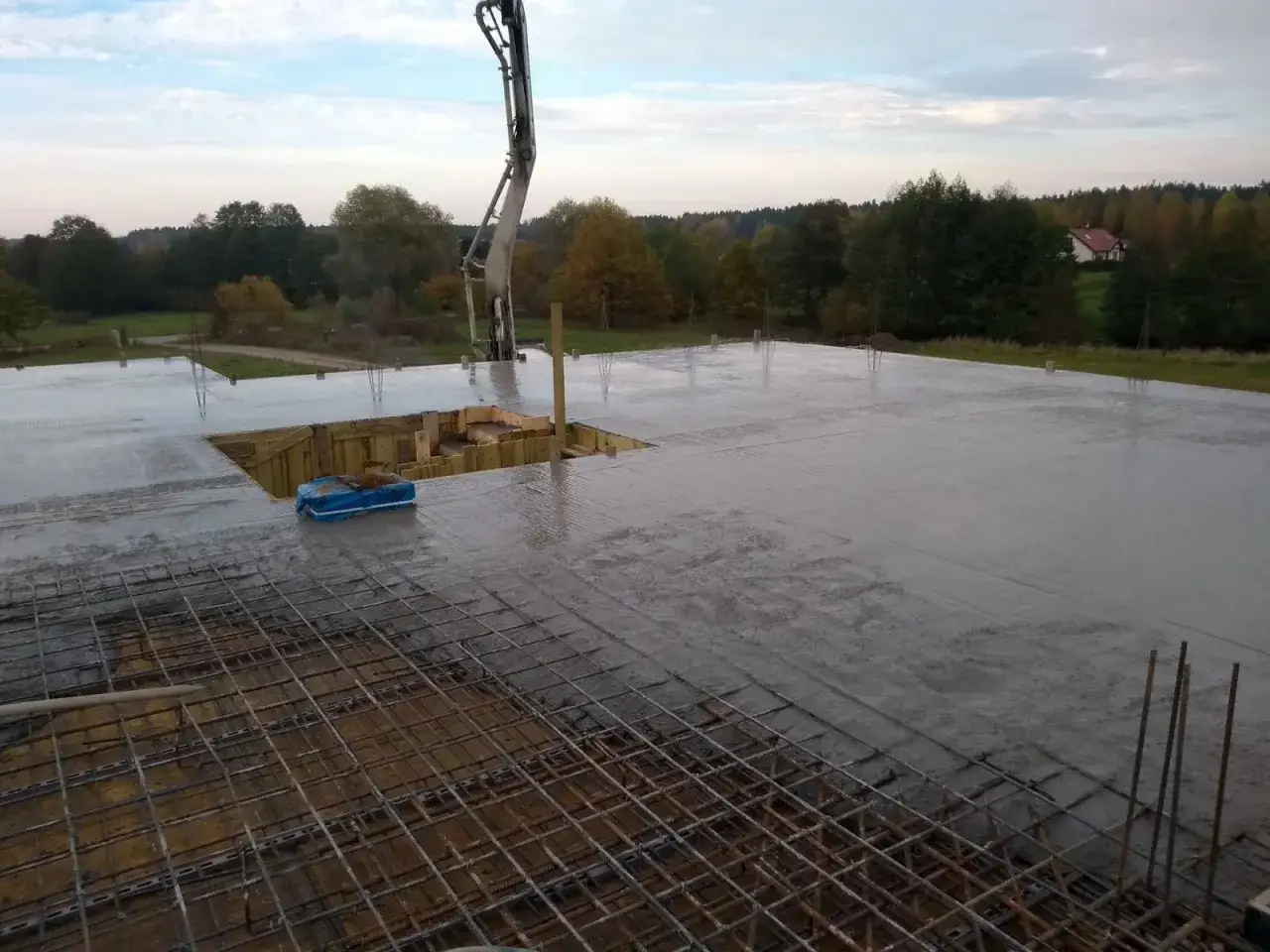 Betoniarka z wysięgnikiem wylewa beton na strop żelbetowy. Widać zbrojenie i szalunki.