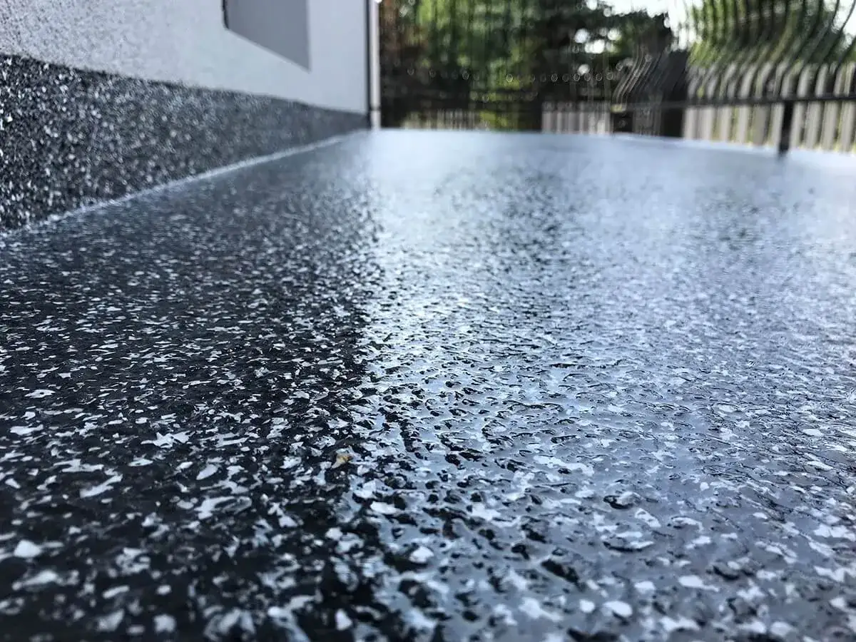 Nowoczesna żywica na balkon cena za metr. Ciemna, błyszcząca powierzchnia z białymi drobinkami, idealna na taras.