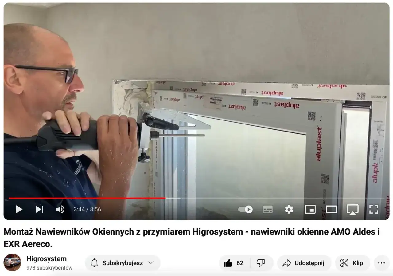 Montaż nawiewników okiennych z przyrządem Higrosystem. Mężczyzna wierci otwory w ramie okna, przygotowując miejsce na nawiewniki.