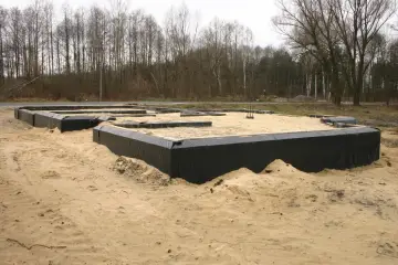 Fundamenty domu w piasku, zabezpieczone czarną folią. Trwa izolacja przeciwwilgociowa fundamentów.